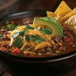 Bowl of chipotle ground beef soup with garnishes and tortilla chips.